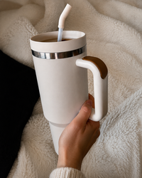 Hand holding a cream insulated handled tumbler filled with coffee while relaxing under a soft blanket at home.