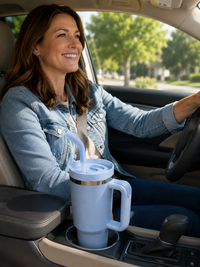 Smiling woman driving with a light blue 40oz tumbler secured in a vehicle cup holder, featuring a reusable straw lid and large-capacity insulated drinkware design for travel-friendly hydration on the go.