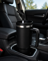 Black 40oz insulated travel tumbler with handle and straw secured in a vehicle cup holder during a daily commute with a clean and professional interior.
