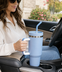 Woman seated in a vehicle holding a light blue travel mug with ergonomic handle and reusable straw, showcasing large-capacity insulated drinkware designed for on-the-go drinking, daily commuting, and secure cup holder compatibility.